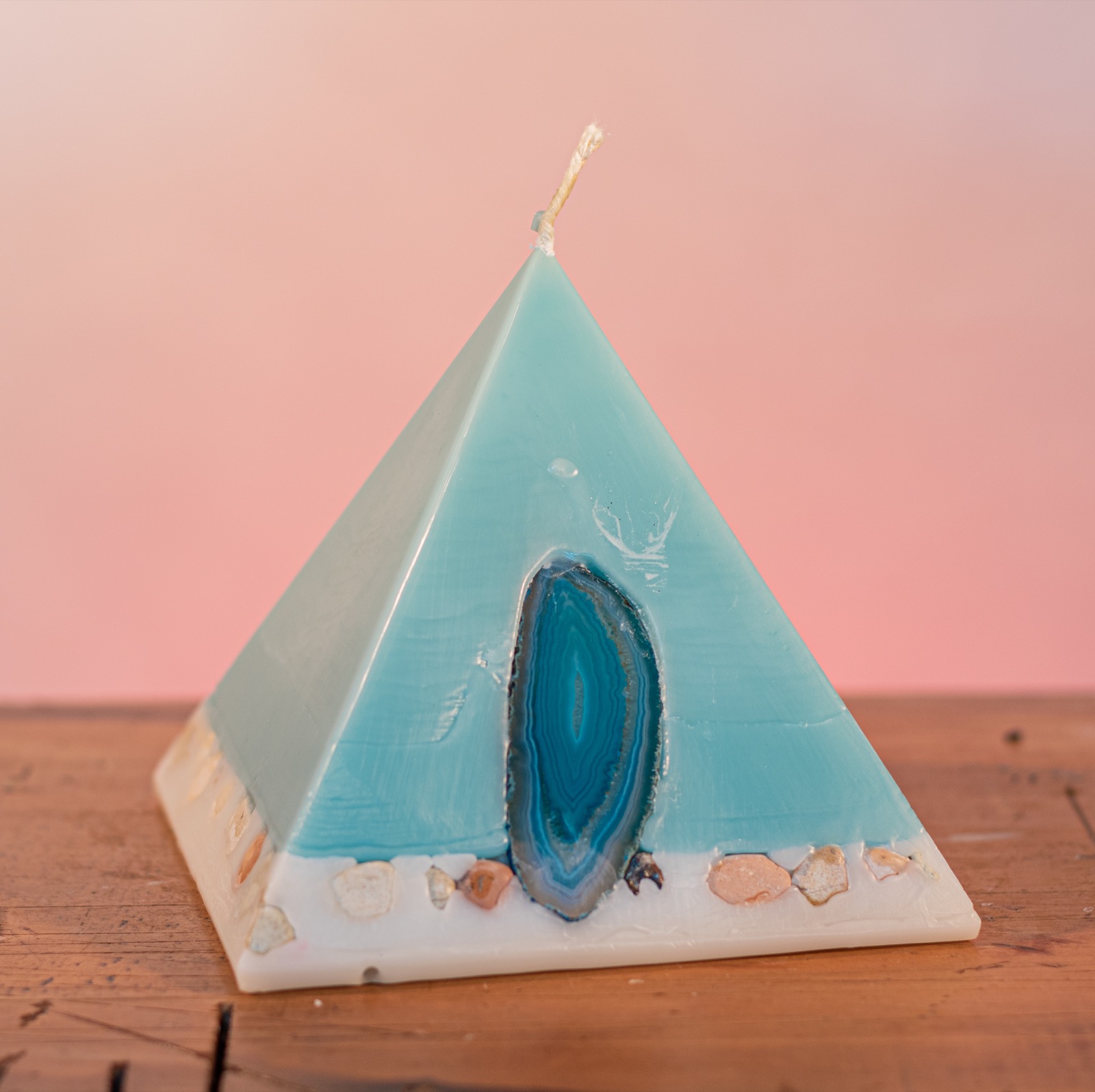 As your pyramid candle burns, the flame illuminates the Agate, revealing the stone's unique variegated patterns, and leaves you with a gorgeous keepsake. Essential oils of Himalayan Patchouli and Sandalwood create a sophisticated scent reminiscent of the swinging 60s' counter-culture. Teal coloured, this elegant candle further features a crisp white base embedded with river pebbles. As your pyramid candle burns, the flame illuminates the Agate, revealing the stone's unique variegated patterns, and leaves you with a gorgeous keepsake. Essential oils of Himalayan Patchouli and Sandalwood create a sophisticated scent reminiscent of the swinging 60s' counter-culture. Teal coloured, this elegant candle further features a crisp white base embedded with river pebbles.